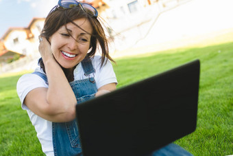 好新闻肖像成人高加索人女人在情感上笔记本快乐有吸引力的女快乐的情绪会说话的朋友会议调用笔记本穿着牛仔裤工作服坐着草公园