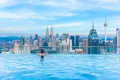 女人放松∞游泳池屋顶前美丽的城市摩天大楼视图(泥马来西亚