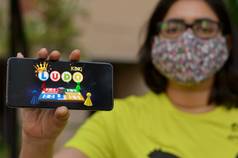 德里印度女孩穿外科手术脸面具显示骰子游戏王游戏应用程序移动电话屏幕由于电晕病毒科维德疾病流感大流行锁用户玩游戏