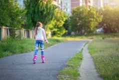 女孩游乐设施粉红色的辊溜冰鞋沥青夏天孩子学习骑辊溜冰鞋滑冰