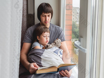 父亲读取书儿子舒适的家庭时间窗台上whi