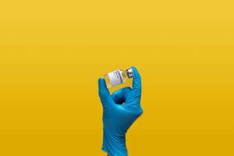 医生实验室穿蓝色的橡胶手套持有冠状病毒疫苗剂量瓶标签孤立的黄色的背景实验室分析测试发明药物疫苗新冠病毒