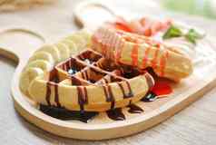美味的华夫格超过草莓糖浆巧克力酱汁一边菜新鲜的草莓切碎香蕉生奶油冰奶油服务可爱的木板