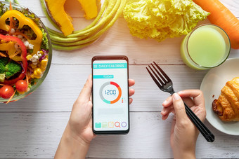 卡路里计数饮食食物控制重量损失概念女人卡路里计数器应用程序智能手机餐厅表格沙拉水果汁面包蔬菜