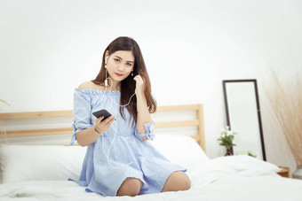 美丽的亚洲女人耳机放松首页坐着床上听音乐应用程序移动电话