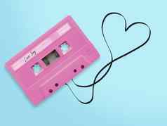 粉红色的音频盒式磁带磁带标签标签爱首歌纠结的磁带丝带心形状孤立的蓝色的背景前视图