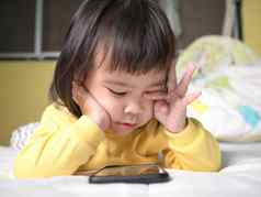 亚洲女孩摩擦眼睛感觉痛苦的看智能手机床上孩子上瘾移动手机