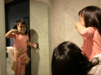 可爱的亚洲孩子女孩刷牙牙齿前面镜子妈妈。早....健康护理概念