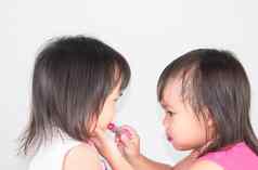 亚洲孩子女孩应用红色的口红嘴唇妹妹白色背景