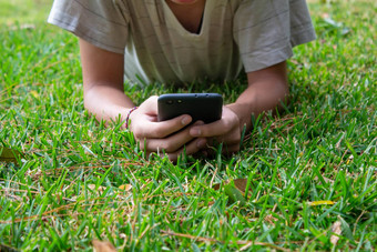 亚洲青少年男孩说谎草地面花园智能手机幸福的