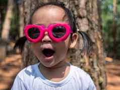 可爱的亚洲孩子女孩穿粉红色的眼镜白色t恤站花园