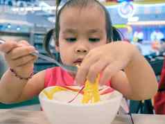 快乐亚洲孩子吃美味的面条手指叉食物法院购物中心
