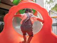 亚洲女孩爬红色的隧道管幻灯片公园操场上玩学习孩子们危险的孩子们概念