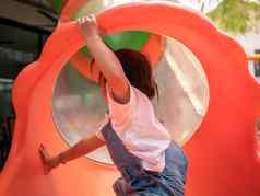 亚洲女孩爬红色的隧道管幻灯片公园操场上玩学习孩子们危险的孩子们概念
