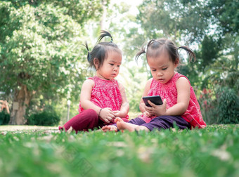亚洲女孩亚裔女孩妹妹坐着<strong>草地</strong>面花园智能手机幸福的妹妹坐着<strong>草地</strong>面