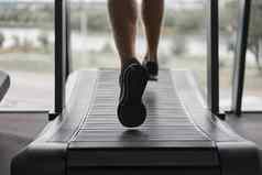 认不出来男人。运行跑步机健身房运动员慢跑室内重量损失锻炼慢跑者运行灰色的墙背景有氧运动培训