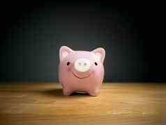 小猪银行储蓄货币概念粉红色的小猪银行微笑脸木表格黑色的背景