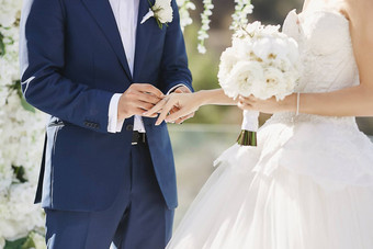 手婚礼环流行的新郎把金环新娘的手指婚礼仪式爱的夫妇女孩婚礼衣服英俊的男人。时尚的蓝色的西装