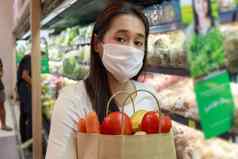 亚洲女人穿保护脸面具持有纸购物袋