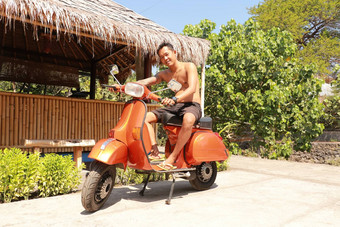 巴厘岛印尼7月尤格风印尼男人。坐着橙色经典维斯帕橙色经典维斯帕橙色维斯帕超级摩托车停人行道上
