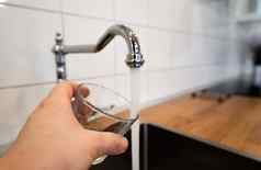 男人手持有空玻璃附近的不锈钢钢厨房利用人倒运行水铬水龙头安全喝适合人类消费适于饮用的饮用