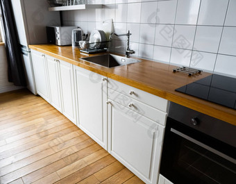 <strong>电器</strong>家具明亮的白色橱柜木工作台面电炊具感应滚刀水龙头水槽菜架硬木地板上光瓷砖现代斯堪的那维亚厨房