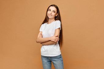 年轻的女人白色空白t恤蓝色的牛仔裤摆姿势折叠手米色背景孤立的模型女孩休闲装模型广告