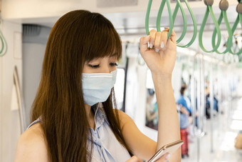 年轻的亚洲女人乘客穿外科手术面具听音乐移动<strong>电话地铁</strong>火车