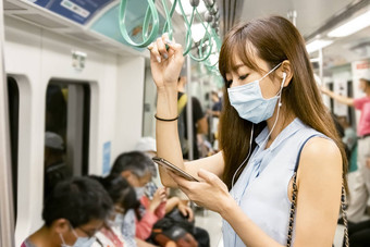 年轻的亚洲女人乘客穿外科手术面具听音乐移动<strong>电话地铁</strong>火车