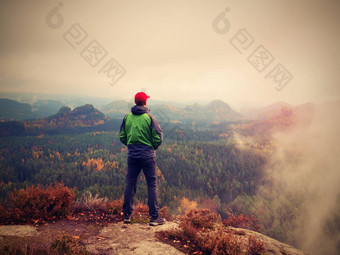 男人。旅游保持锋利的岩石峰徒步旅行者红色的帽绿色夹克享受视图