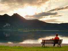 男人。坐在腿板凳上Azure山湖男人。放松看高山峰阿尔卑斯山脉