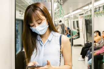 年轻的亚洲女人乘客穿外科手术面具移动<strong>电话地铁</strong>火车