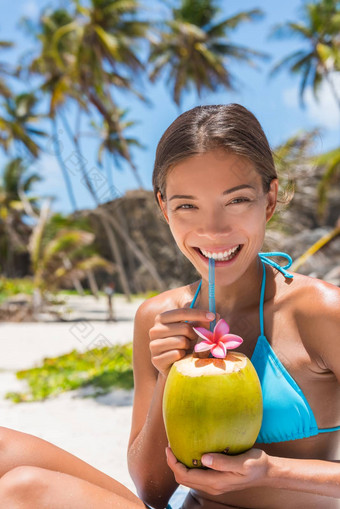 美丽的亚洲比基尼女人喝新鲜的椰子水直接水果稻草海滩多民族的女孩微笑相机肖像完美的牙齿喝着水合作用汁食物
