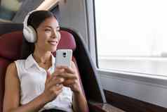 女人火车听音乐智能手机人生活方式年轻的城市女商人电话应用程序无线耳机听有声读物亚洲女孩享受旅行业务类