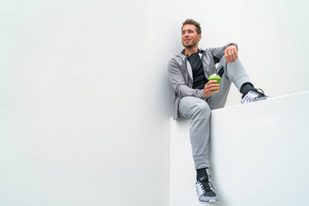 健康的体育运动男人。喝绿色奶昔培训健身房运动服运动裤户外运动员坐着放松运动后