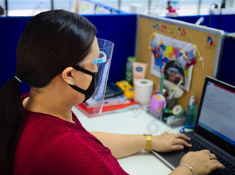 年轻的美丽的亚洲女人穿外科手术面具脸盾保护科维德工作办公室