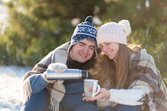 年轻的夫妇爱喝热喝热水瓶坐着冬天森林塞温暖的舒适的地毯享受自然的家伙倒喝热水瓶杯