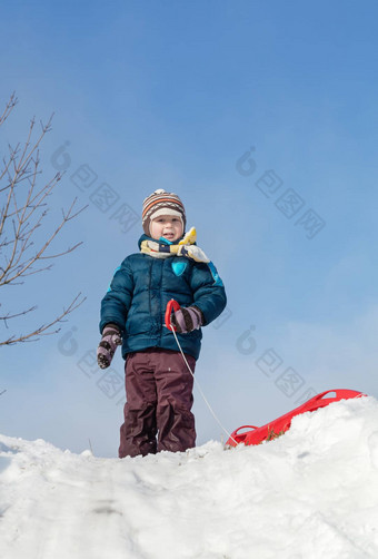 男孩站红色的塑料雪橇雪山