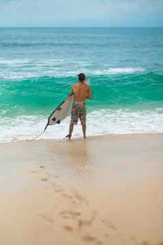 冲浪者冲浪男人。冲浪板走桑迪热带海滩健康的生活方式水活动水体育运动美丽的海洋