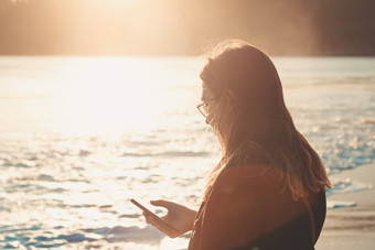 年轻的女人检查手机海滩日落复制空间色彩斑斓的音调