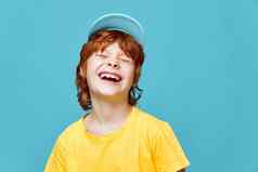 快乐的红色头发的人男孩笑关闭眼睛蓝色的帽黄色的t恤裁剪视图