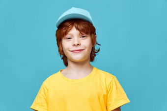 微笑红色头发的人男孩蓝色的帽黄色的T恤裁剪视图