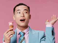 快乐亚洲男人。吃冰奶油粉红色的背景蓝色的经典西装特写镜头