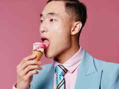 亚洲男人。吃冰奶油粉红色的背景裁剪视图