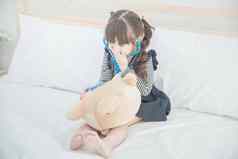可爱的亚洲女孩享受玩医生医生玩具集可爱的娃娃坐着床上儿童卧室首页
