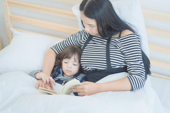 快乐爱的家庭漂亮的年轻的妈妈。阅读床上时间故事书女儿卧室