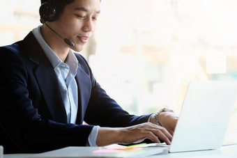 亚洲商人耳机移动PC看好网络研讨会咨询客户端距离学习语言使笔记快乐男人。参与在线会议