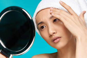 女人亚洲外观触摸脸清洁皮肤镜子蓝色的背景