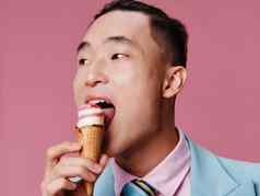 快乐亚洲男人。吃冰奶油粉红色的背景蓝色的经典西装裁剪视图