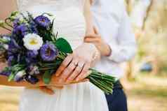新郎轻轻拥抱新娘橄榄格罗夫新娘持有花束蓝色的花特写镜头